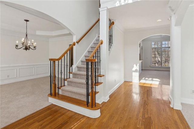 stairs with arched walkways, a decorative wall, a wainscoted wall, wood finished floors, and ornamental molding