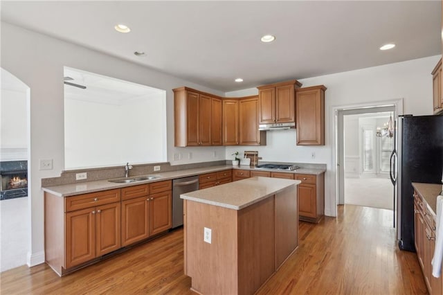 kitchen with light wood finished floors, a kitchen island, appliances with stainless steel finishes, under cabinet range hood, and a sink