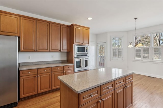 kitchen with stainless steel appliances, brown cabinetry, decorative light fixtures, and light wood-style floors