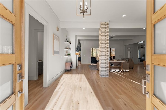 entryway with beamed ceiling, a notable chandelier, decorative columns, and light wood-type flooring