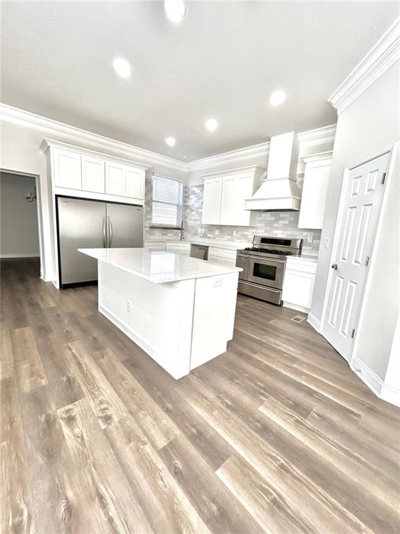 kitchen with premium range hood, a kitchen island, appliances with stainless steel finishes, tasteful backsplash, and white cabinets