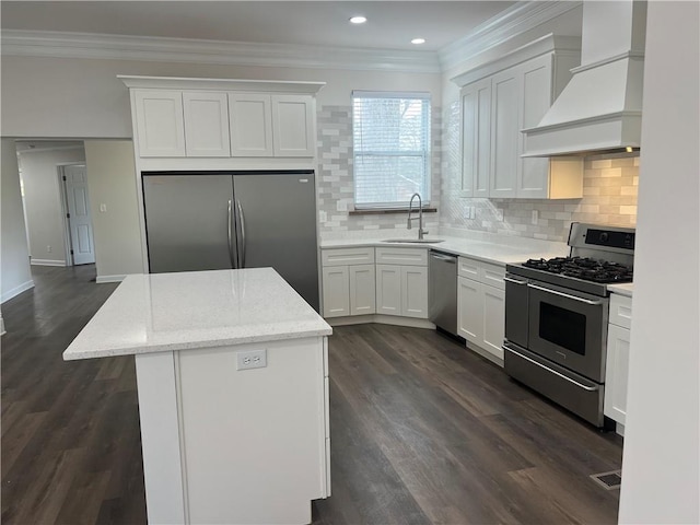 kitchen featuring ornamental molding, custom range hood, a sink, a kitchen island, and appliances with stainless steel finishes