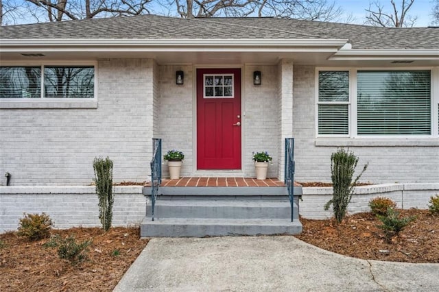 view of exterior entry with brick siding and a shingled roof