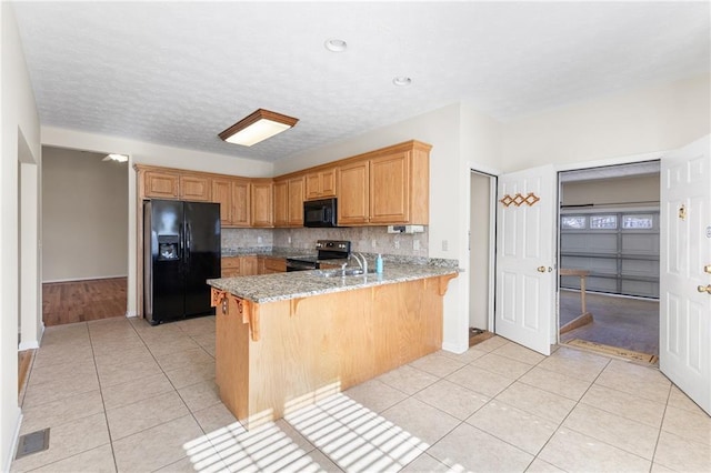 kitchen featuring black appliances, light stone counters, a peninsula, and light tile patterned flooring