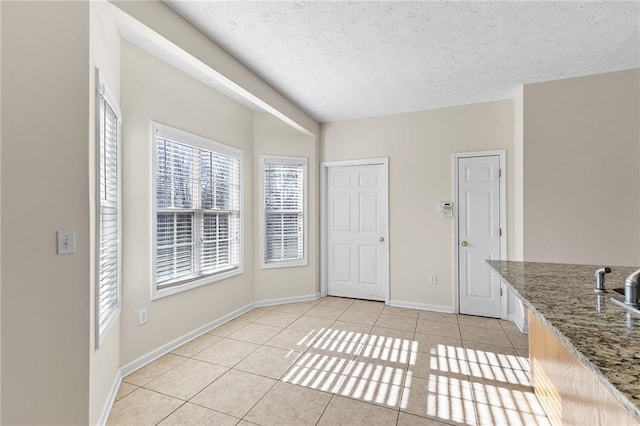 interior space featuring stone counters, a textured ceiling, baseboards, and light tile patterned floors