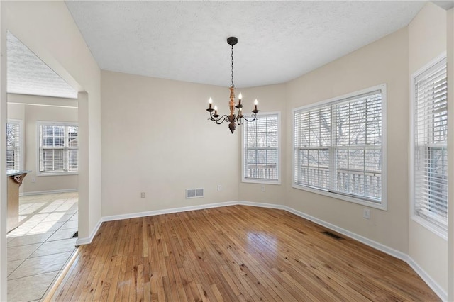 unfurnished dining area with light wood-style floors, visible vents, baseboards, and an inviting chandelier