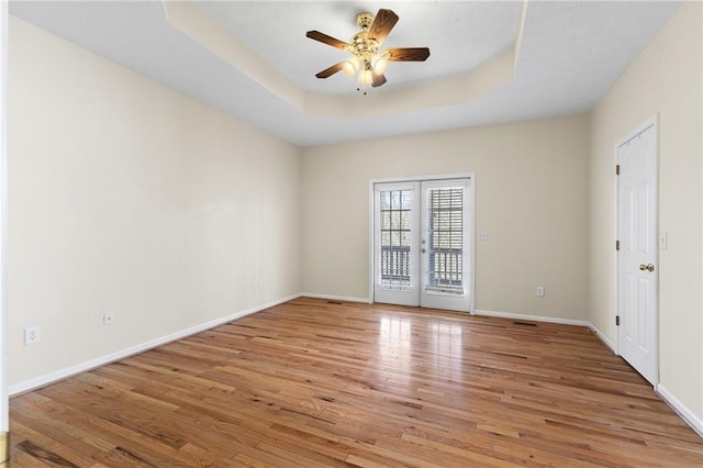 spare room featuring light wood-style flooring, a ceiling fan, baseboards, french doors, and a raised ceiling