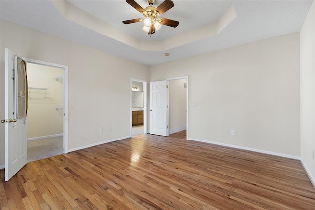 unfurnished bedroom featuring light wood-type flooring, a tray ceiling, and baseboards