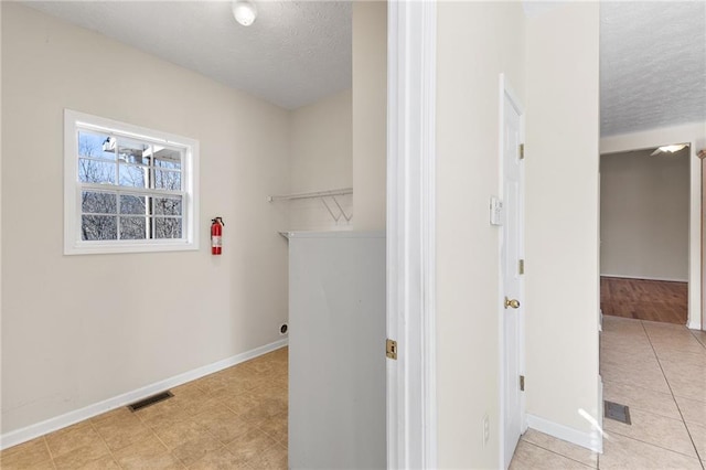 washroom with a textured ceiling, visible vents, and baseboards