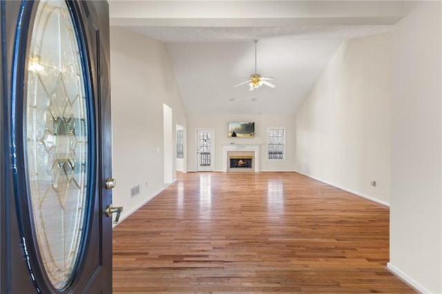 unfurnished living room featuring a warm lit fireplace, wood finished floors, visible vents, baseboards, and a ceiling fan