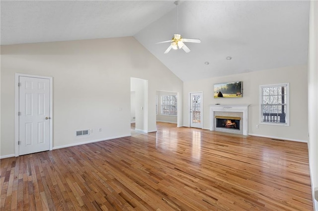 unfurnished living room featuring a warm lit fireplace, plenty of natural light, visible vents, and light wood-style floors