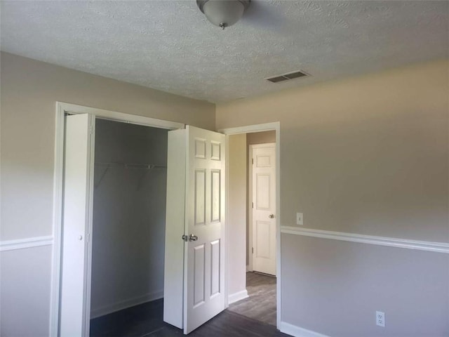 unfurnished bedroom with dark hardwood / wood-style floors, a textured ceiling, and a closet