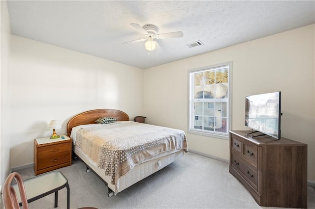 bedroom featuring ceiling fan, light colored carpet, and a textured ceiling