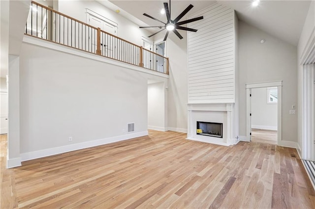 unfurnished living room featuring ceiling fan, a large fireplace, high vaulted ceiling, and light wood-type flooring