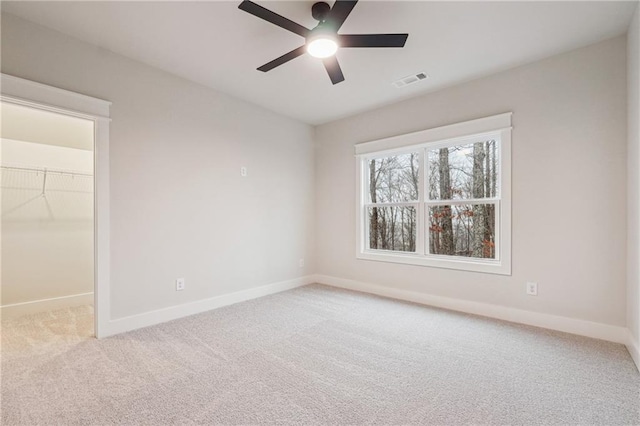 unfurnished bedroom with a spacious closet, light colored carpet, a closet, and ceiling fan