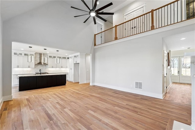 unfurnished living room with light hardwood / wood-style flooring, high vaulted ceiling, french doors, and ceiling fan