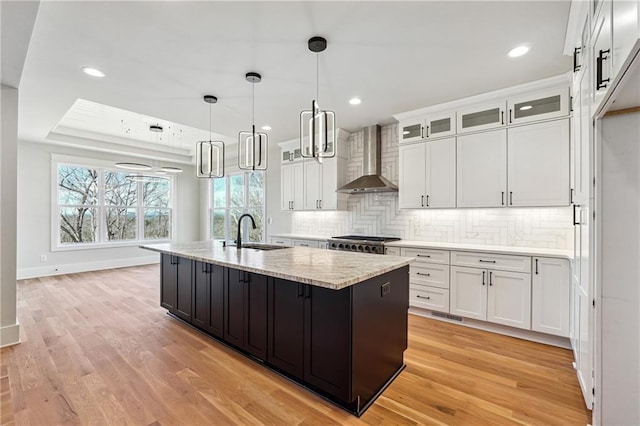 kitchen with white cabinetry, wall chimney range hood, sink, and an island with sink