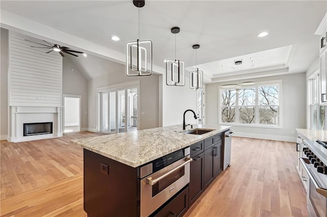 kitchen featuring sink, appliances with stainless steel finishes, a kitchen island with sink, a tray ceiling, and decorative light fixtures