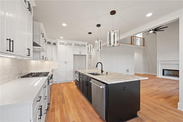 kitchen with appliances with stainless steel finishes, pendant lighting, sink, white cabinets, and a kitchen island with sink