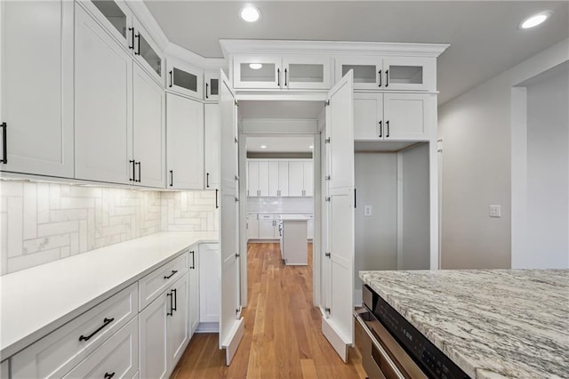 kitchen featuring backsplash, white cabinets, light stone counters, and light hardwood / wood-style flooring