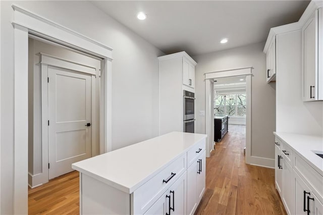 kitchen with white cabinetry, double oven, and light hardwood / wood-style floors