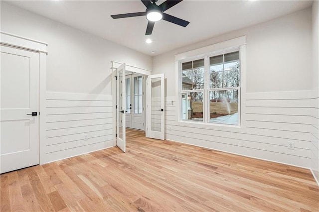 unfurnished room with ceiling fan, wooden walls, and light wood-type flooring