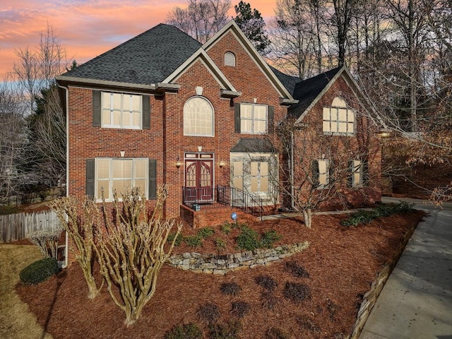 view of front facade with french doors, fence, brick siding, and roof with shingles