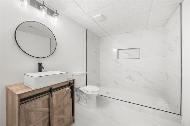 bathroom with vanity, a paneled ceiling, toilet, and tiled shower