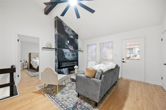 living room featuring wood-type flooring, high vaulted ceiling, beamed ceiling, ceiling fan, and a fireplace