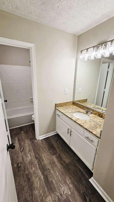 bathroom with a textured ceiling, wood finished floors, vanity, baseboards, and toilet