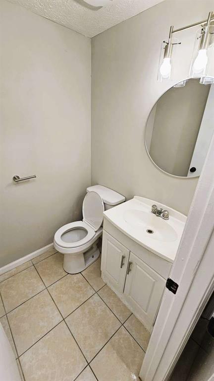half bath with toilet, a textured ceiling, tile patterned flooring, and vanity