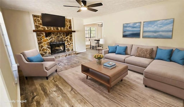 living area featuring a textured ceiling, a stone fireplace, a ceiling fan, and wood finished floors