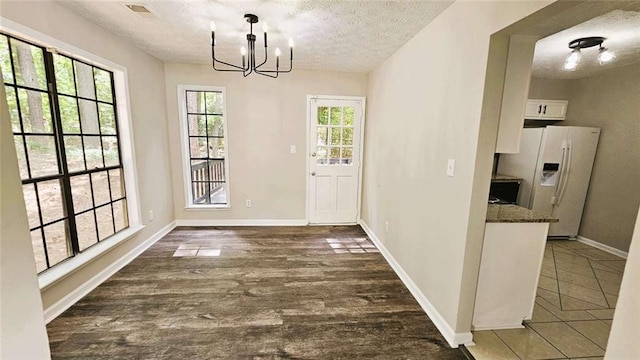 unfurnished dining area with a textured ceiling, visible vents, baseboards, dark wood-style floors, and a notable chandelier