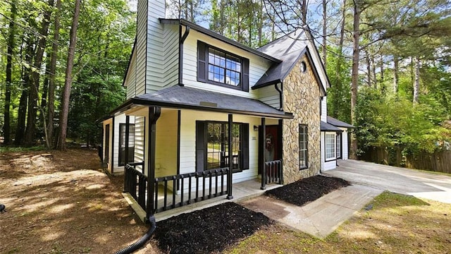 view of front of home with a porch, roof with shingles, a chimney, and stone siding
