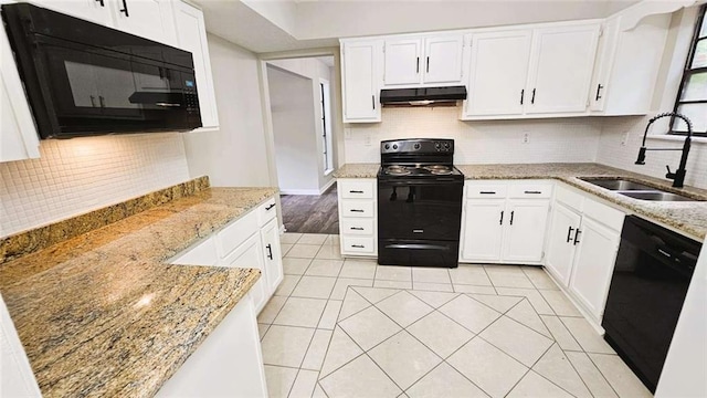 kitchen with under cabinet range hood, light stone countertops, a sink, and black appliances