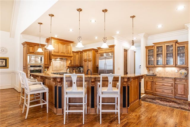 5352 Lacosta Ln, Alpharetta, GA 30022 - kitchen with built in appliances, brown cabinetry, decorative backsplash, dark wood-style flooring, and crown molding