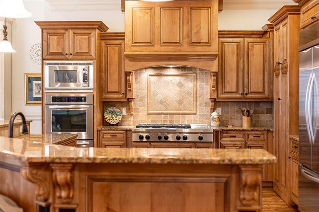 5352 Lacosta Ln, Alpharetta, GA 30022 - kitchen featuring appliances with stainless steel finishes, brown cabinetry, light stone countertops, light wood-style flooring, and ornamental molding