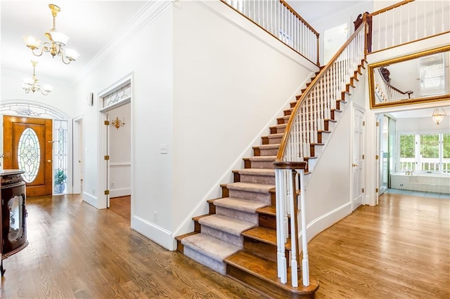 entryway with an inviting chandelier, crown molding, wood finished floors, baseboards, and stairway