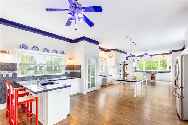 kitchen featuring ceiling fan, a sink, freestanding refrigerator, a peninsula, and white cabinetry