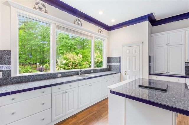 kitchen featuring backsplash, white cabinetry, a sink, and wood finished floors