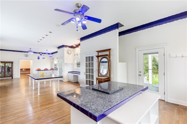kitchen with crown molding, dark countertops, light wood-style floors, ceiling fan, and a center island