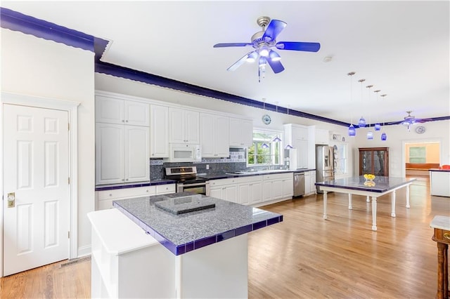 kitchen featuring ceiling fan, appliances with stainless steel finishes, white cabinetry, tasteful backsplash, and a kitchen island
