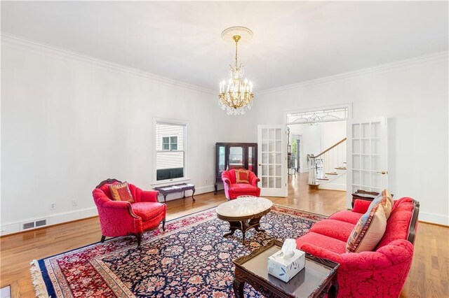 living room with crown molding, a notable chandelier, french doors, stairs, and visible vents