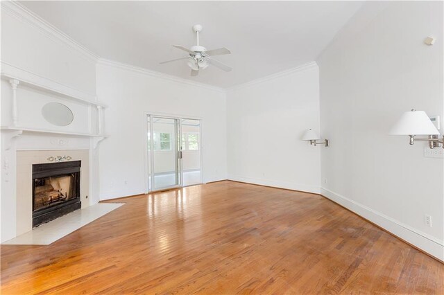 unfurnished living room featuring ceiling fan, a fireplace with flush hearth, ornamental molding, and wood finished floors