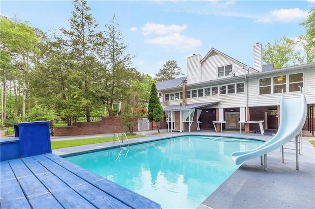 outdoor pool featuring fence, a water slide, and a deck