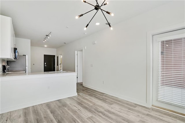 unfurnished living room featuring an inviting chandelier, light hardwood / wood-style flooring, and sink