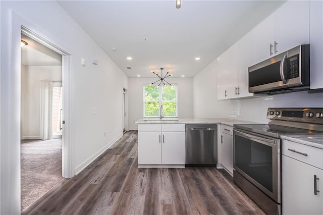 kitchen featuring sink, dark hardwood / wood-style flooring, kitchen peninsula, white cabinets, and appliances with stainless steel finishes