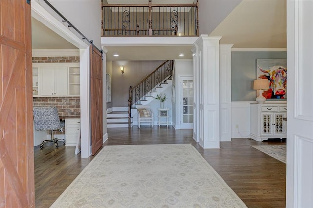 foyer entrance featuring dark wood-type flooring, wainscoting, crown molding, and a high ceiling