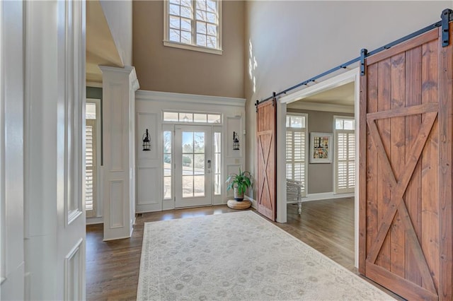 entryway with dark wood-type flooring, ornamental molding, a towering ceiling, and a barn door