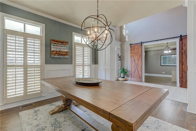 dining room with a wainscoted wall, a barn door, ornamental molding, and visible vents